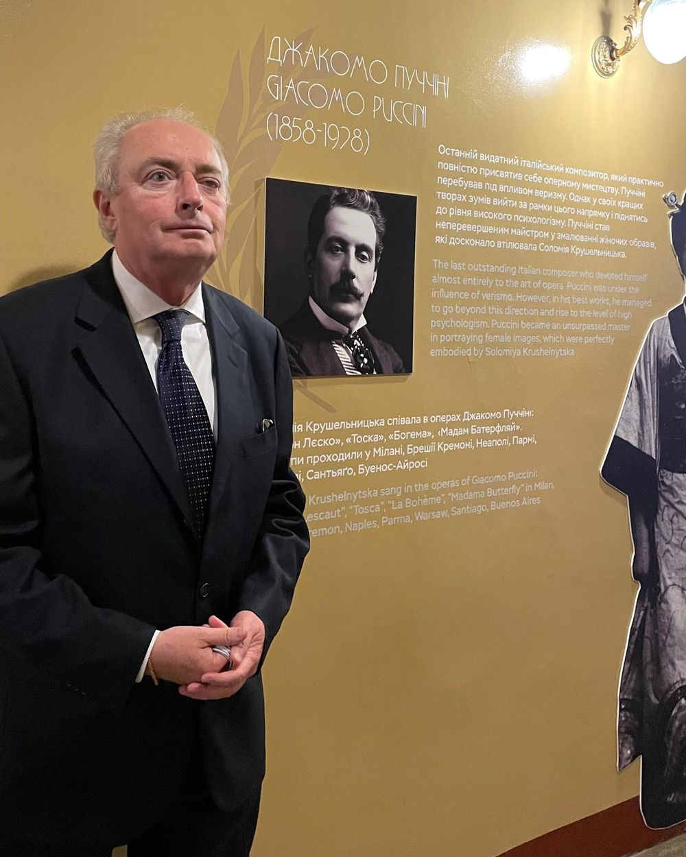 Franco Moretti, in abito scuro, accanto a un pannello dedicato a Giacomo Puccini